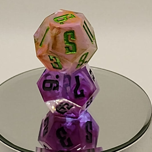 Two polyhedral dice, one pink with green numbers and one purple with black numbers, held in front of a mirror.