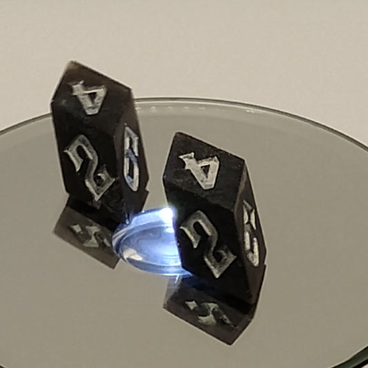 Black polyhedral dice with white numbers on a reflective surface