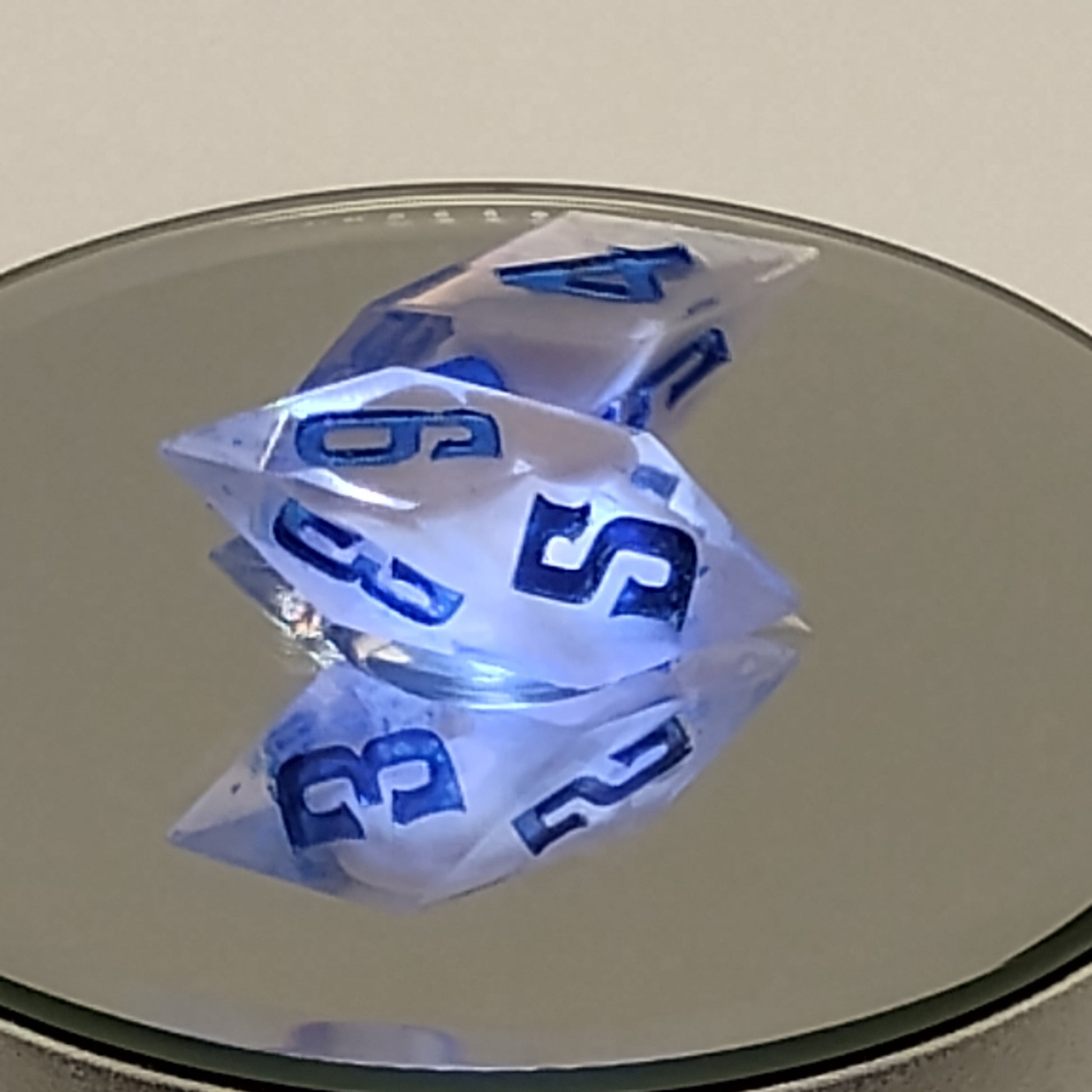 Three polyhedral dice with blue numbers on a reflective surface