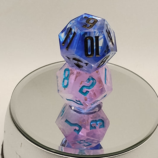 Two polyhedral dice, one blue and one pink with black numbers, on a reflective surface.