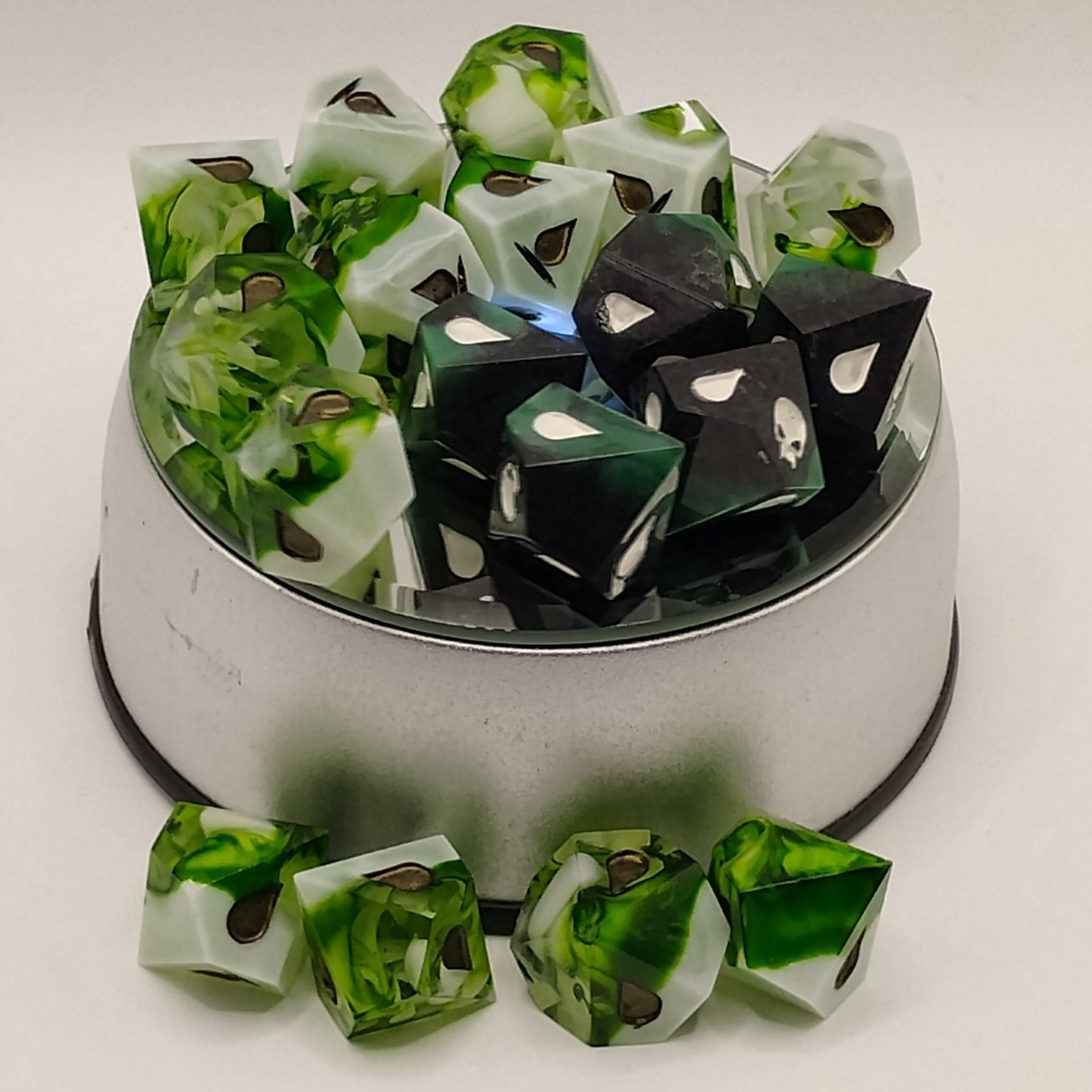 Set of green and black dice with a metal container on a white background