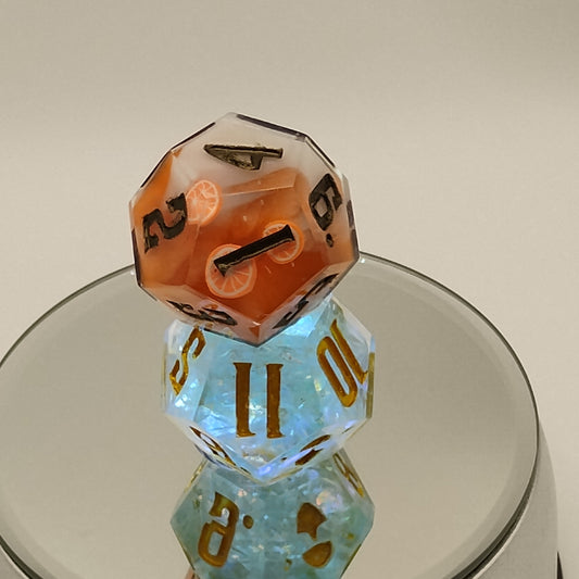 Two polyhedral dice, one orange and one blue, with a glass container on a plain background.
