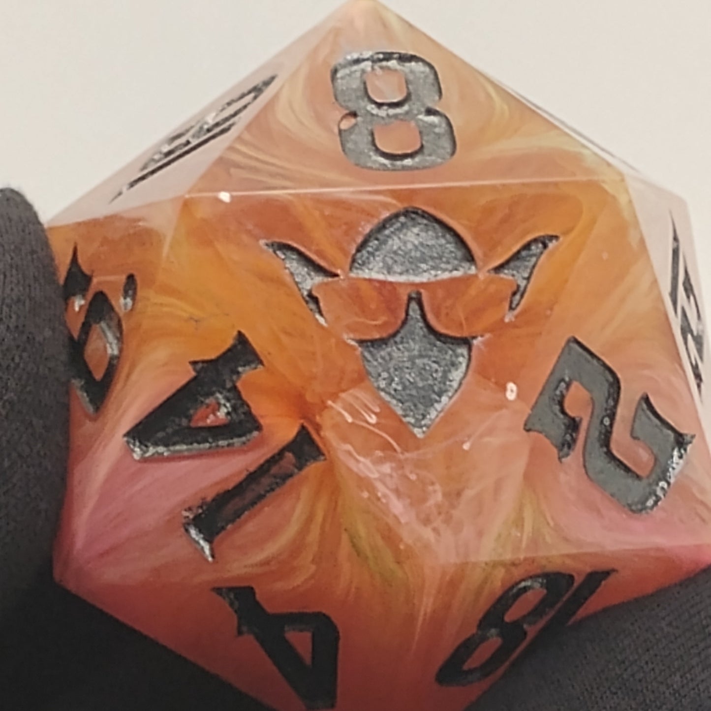 Polyhedral dice with orange and black numbers held by a gloved hand